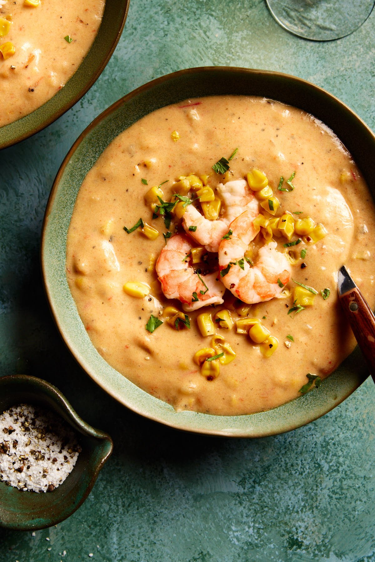 a close up shot of chowder in a bowl topped with shrimp and corn 