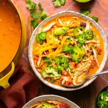 a bowl of creamy chicken tortilla soup in a bowl topped with avocado, cilantro, and jalapeno slices.