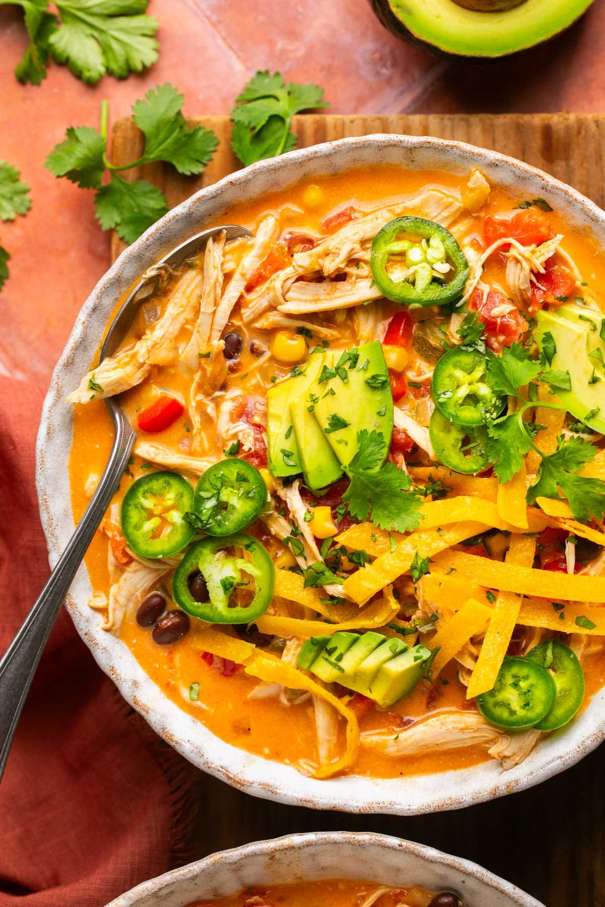 a bowl of creamy chicken tortilla soup in a bowl topped with avocado, cilantro, and jalapeno slices. 