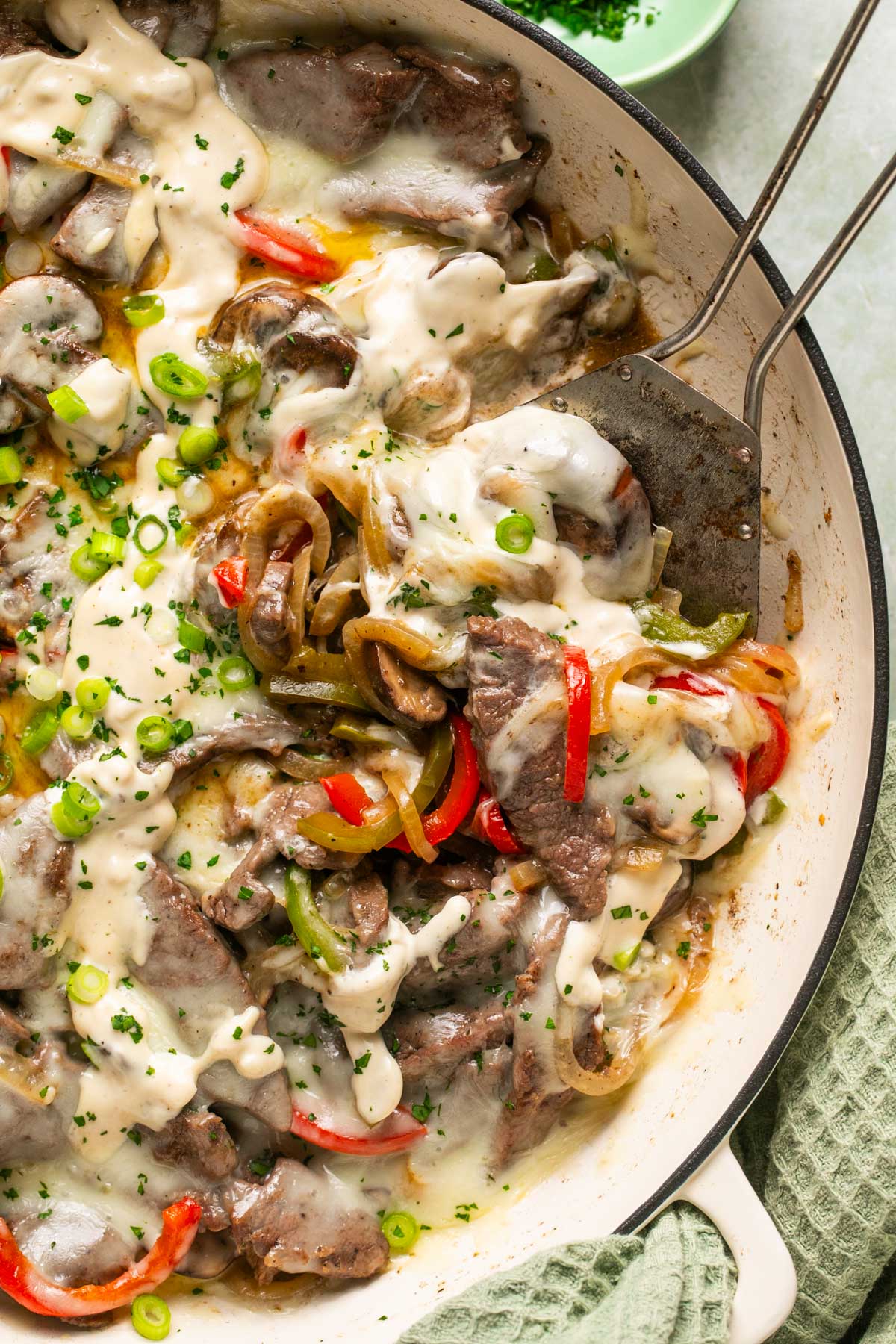 side view of steak, peppers, and cheese in a skillet with a metal spatula