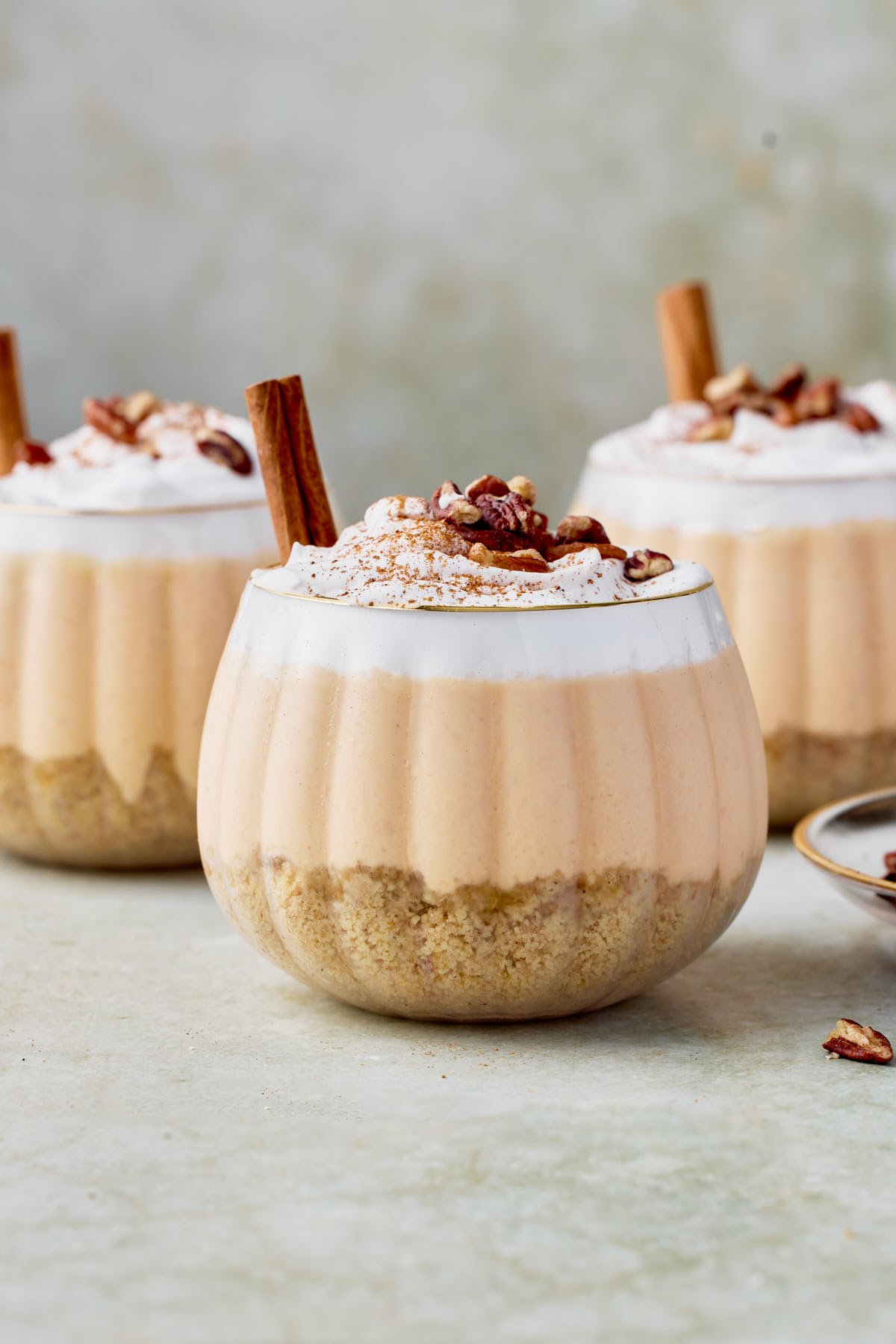 three no-bake pumpkin cheesecake jars topped with whipped cream, cinnamon and a cinnamon stick