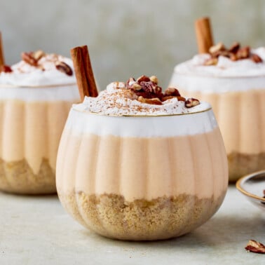 three no-bake pumpkin cheesecake jars topped with whipped cream, cinnamon and a cinnamon stick