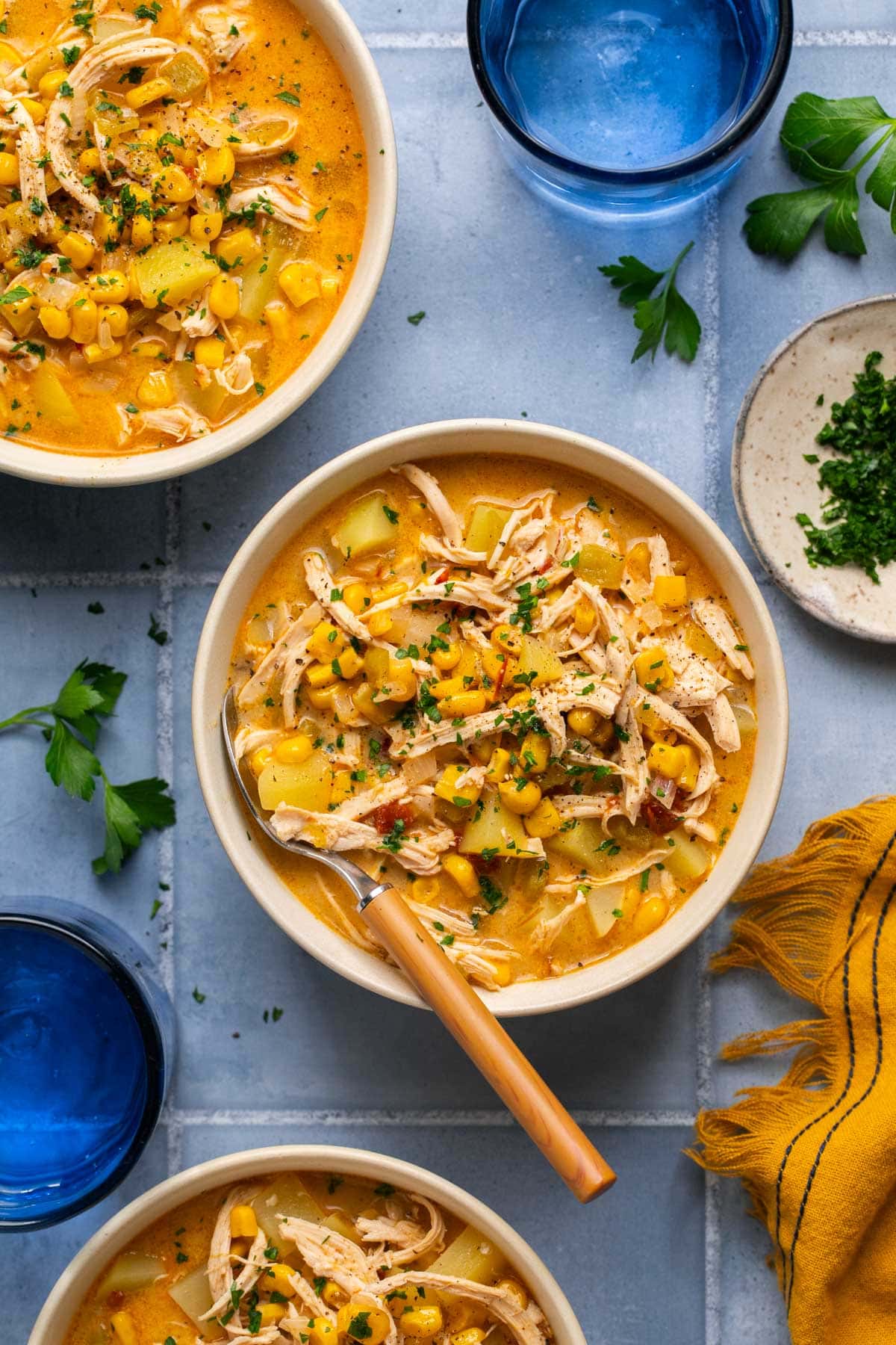 an overhead shot of three bowls. of southwest chicken corn chowder on a blue surface 