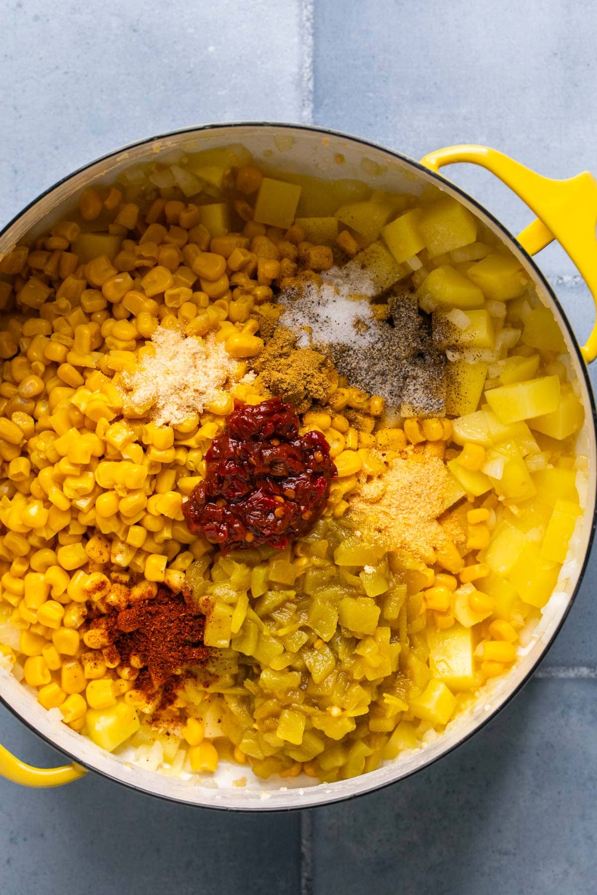 chicken and spices added to a dutch oven with potatoes and veggies