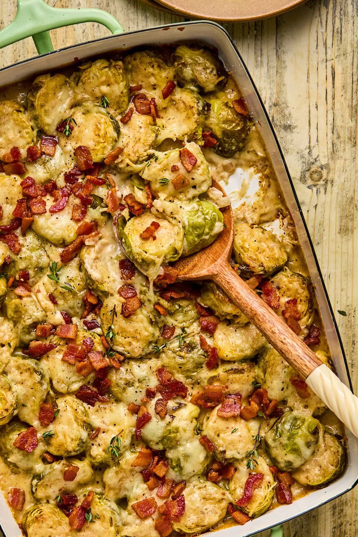 brussels sprouts gratin in a baking dish with a wooden spoon resting inside. 