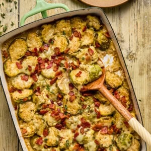 brussels sprouts gratin in a baking dish with a wooden spoon resting inside.