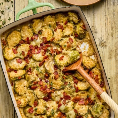 brussels sprouts gratin in a baking dish with a wooden spoon resting inside.