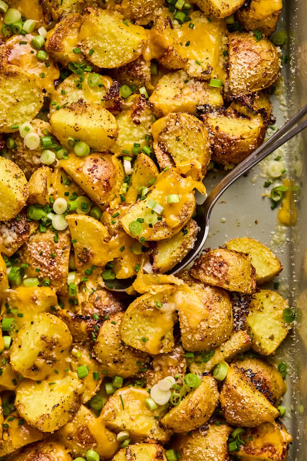 scooping cheesy ranch potatoes out of a baking sheet