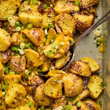 scooping cheesy ranch potatoes out of a baking sheet