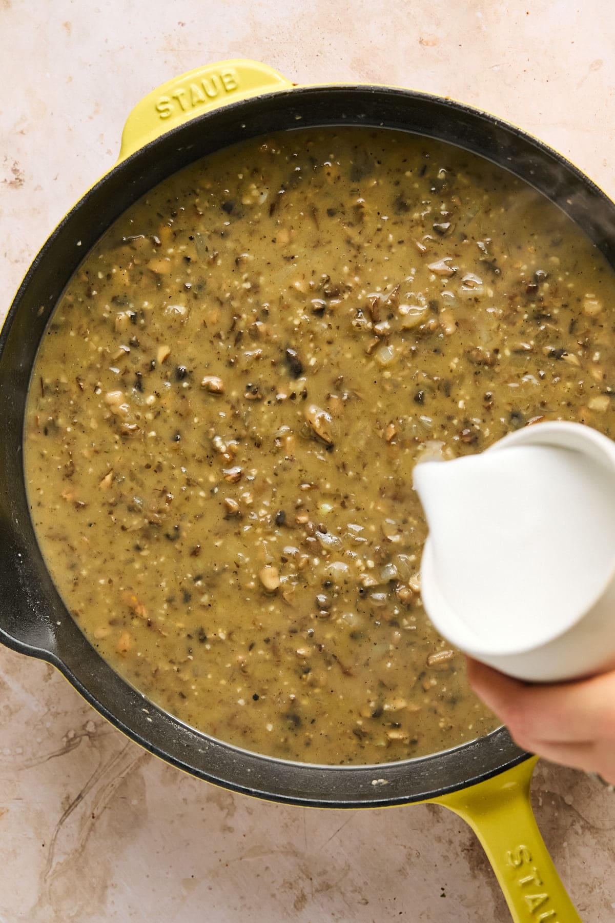 pouring milk into a pan of veggies and broth.