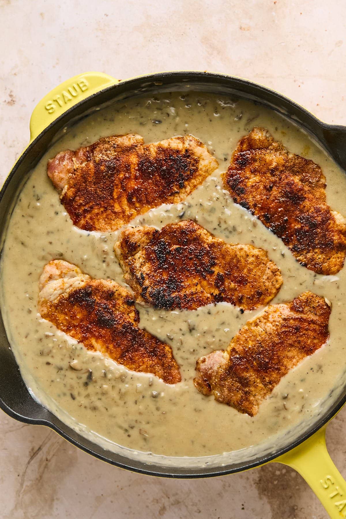 pork chops resting inside of a pan with sauce