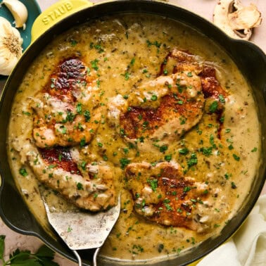 cream of mushroom pork chops in a skillet with sauce and fresh herbs.