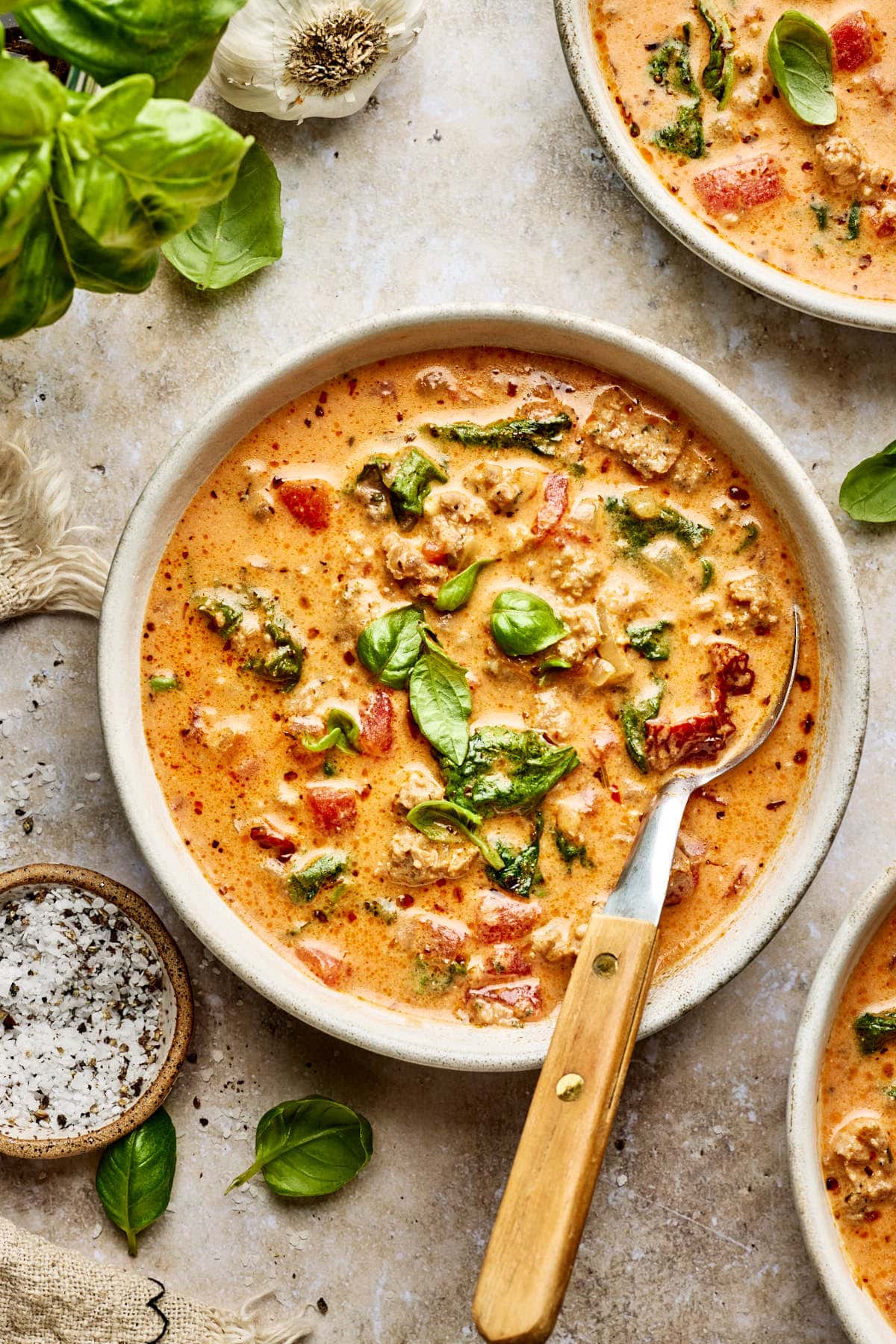 bowls of italian sausage soup with spoons resting on the side.