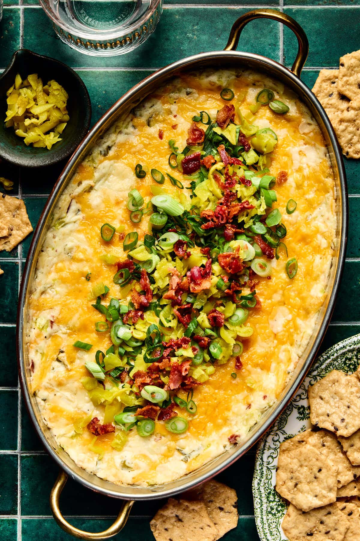 hot pepperoncini dip in a baking dish topped with bacon, green onions, and cheese