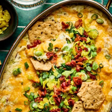 hot pepperoncini dip in a baking dish topped with bacon, green onions, and cheese