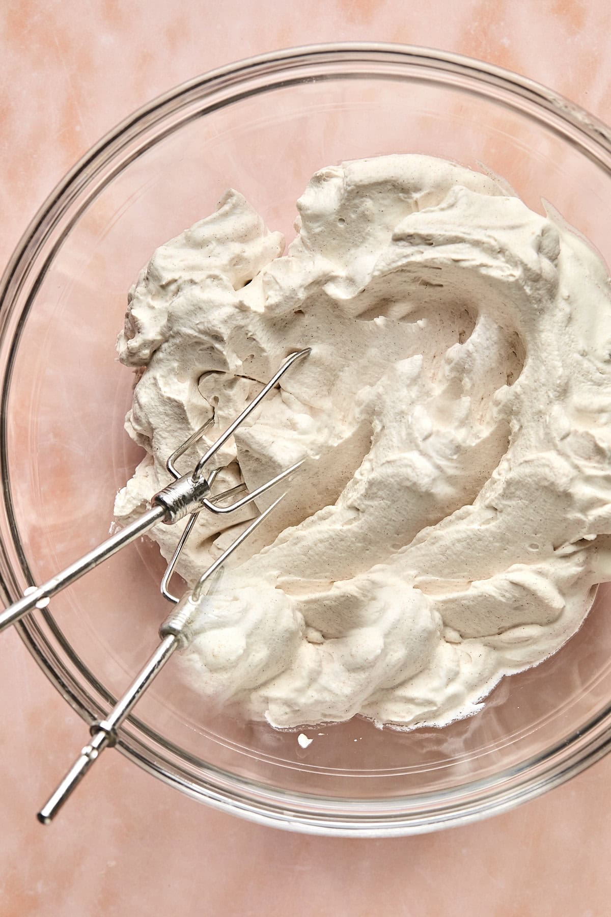 a bowl of whipped cream with hand beaters resting inside. 