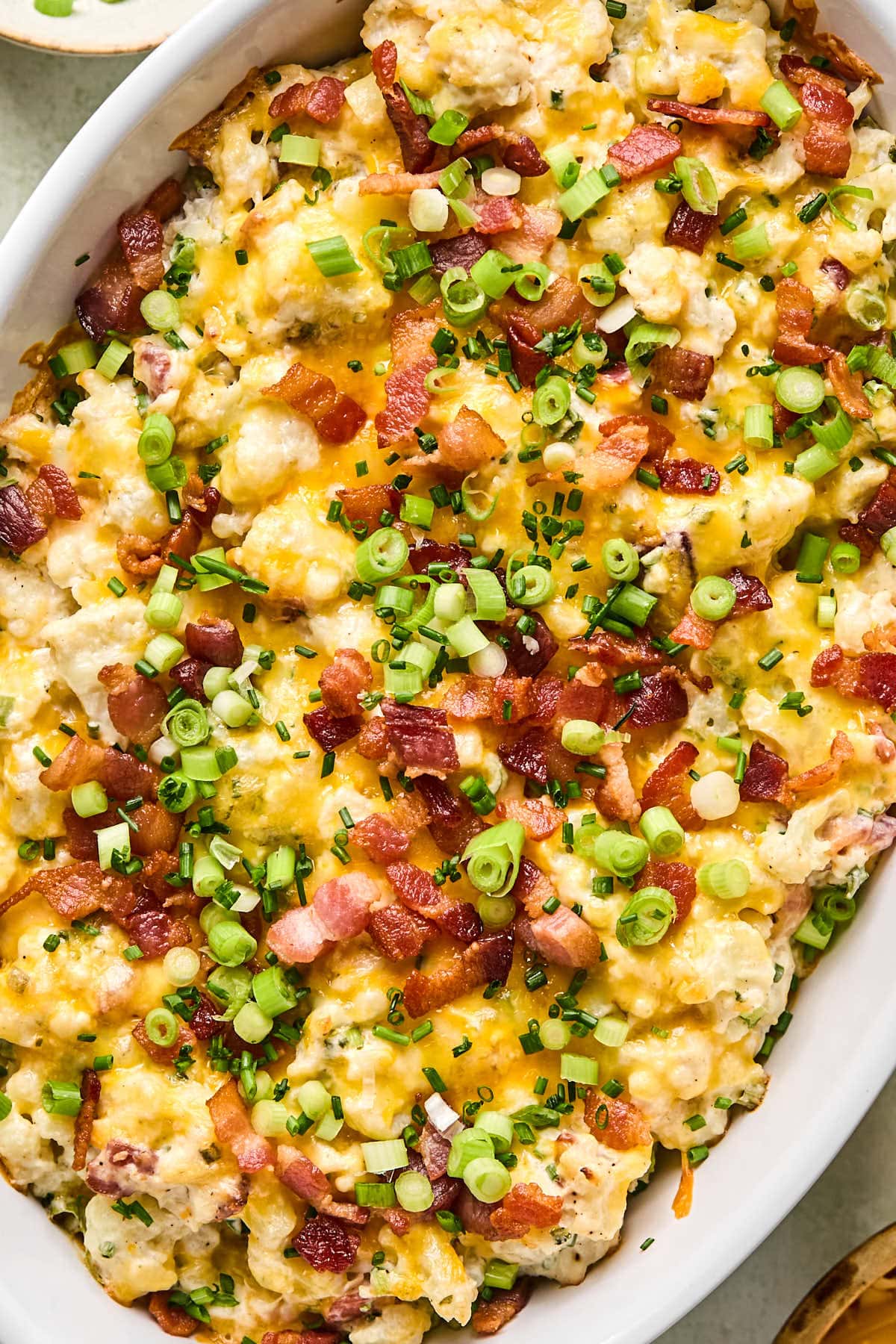 a close up to show the top of the loaded cauliflower casserole with bacon, green onions, and chives on top