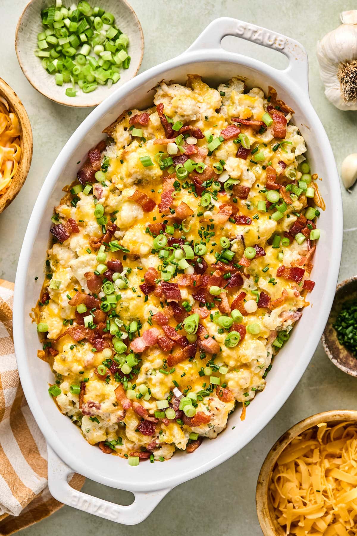 loaded cauliflower casserole in a white baking dish topped with chopped green onions and bacon