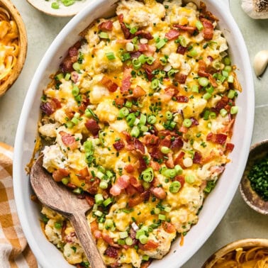 loaded cauliflower casserole in a white baking dish topped with chopped green onions and bacon