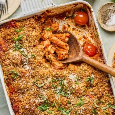 chicken parmesan casserole in a baking dish with a wooden spoon resting inside.