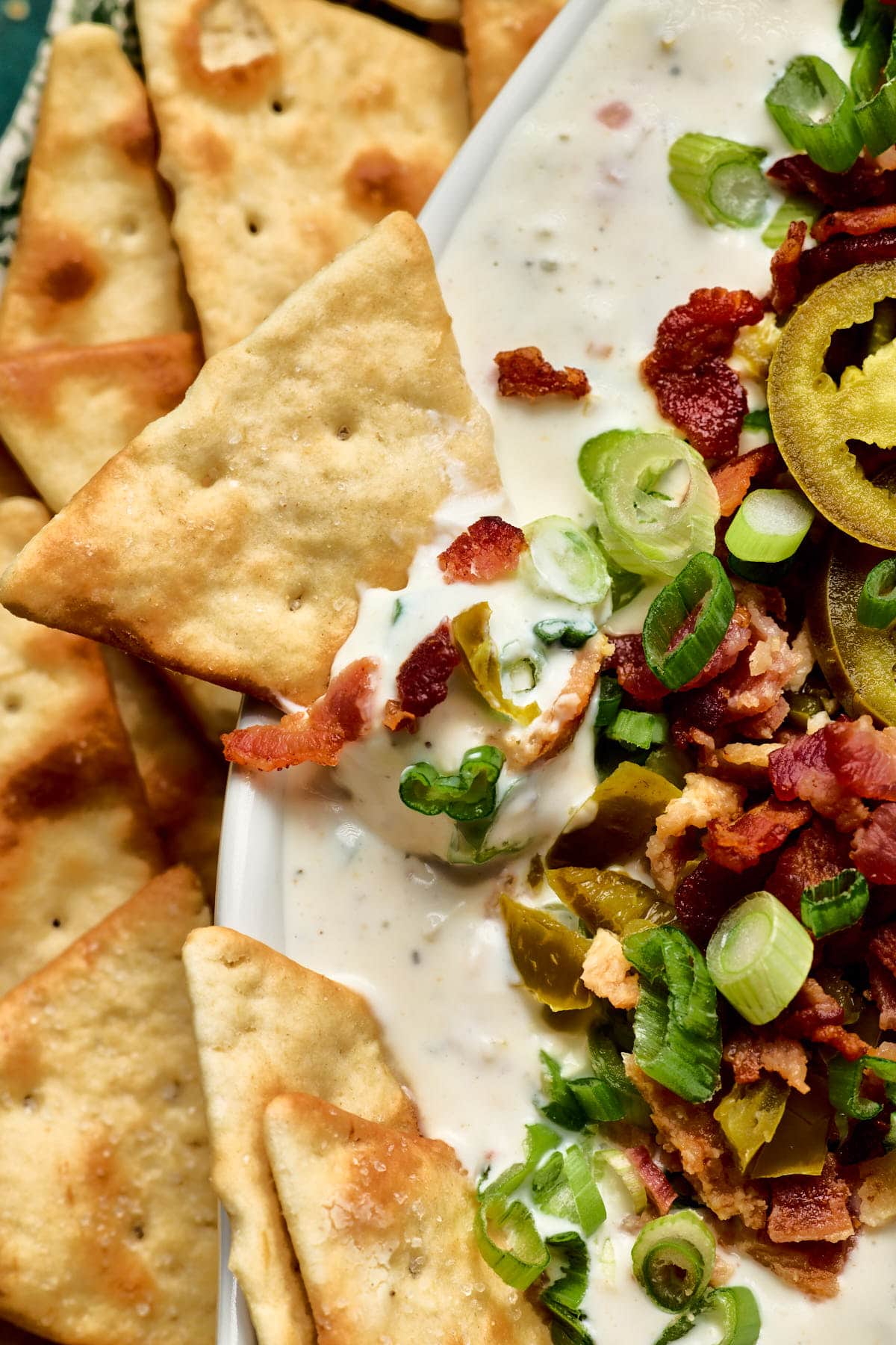 a close up of a cracker dipping into jalapeno ranch dip