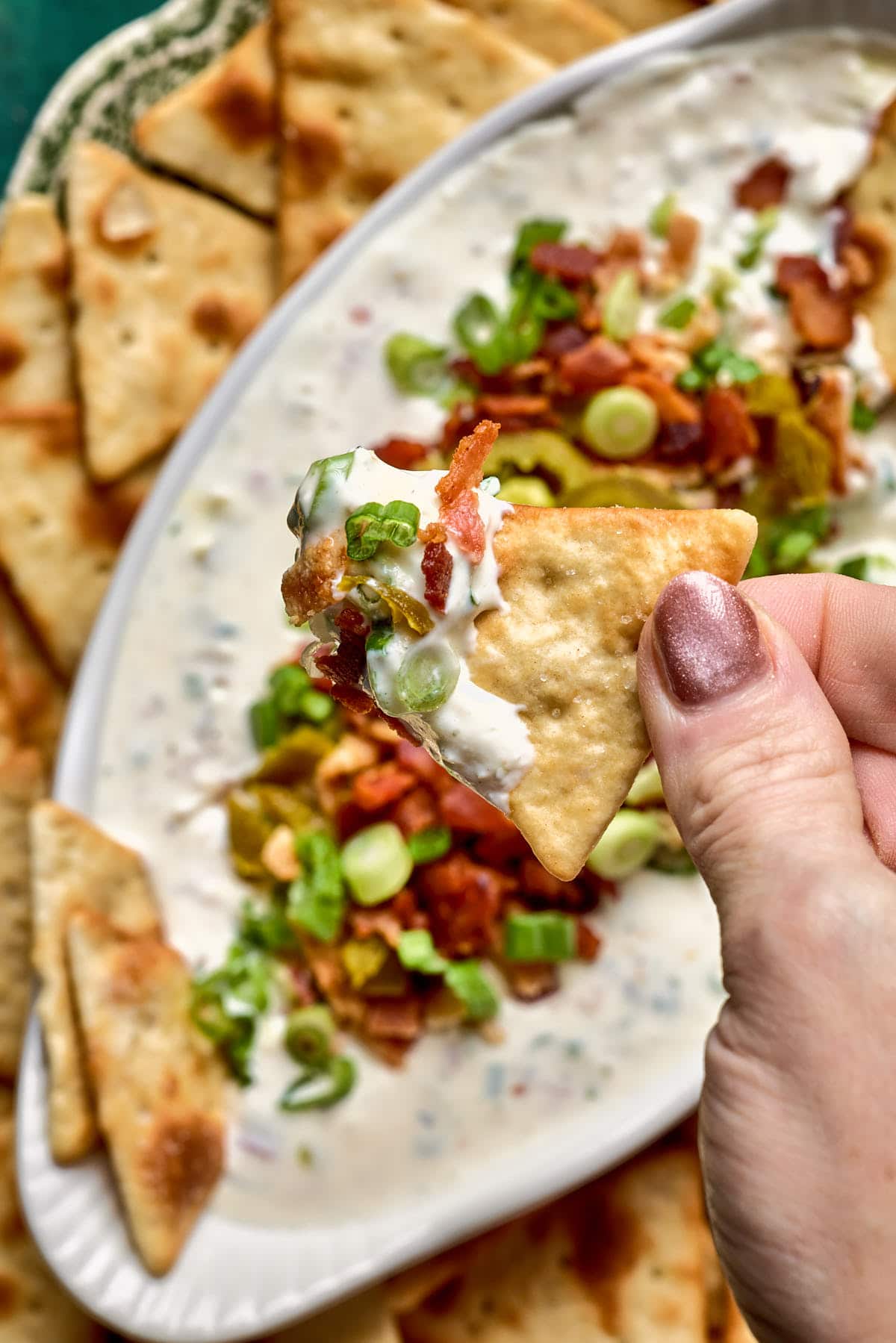 a hand holding a cracker topped with dip 