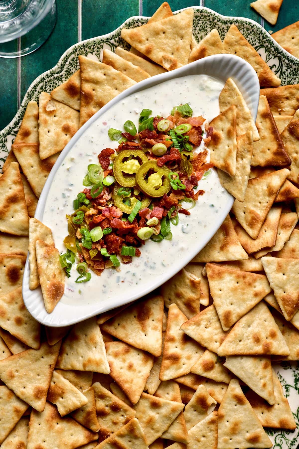 jalapeno ranch dip topped with green onions, jalapenos, and bacon in a dish next to crackers. 