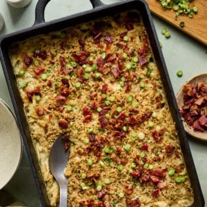 million dollar chicken casserole in a black baking dish with a metal spoon resting on the side.