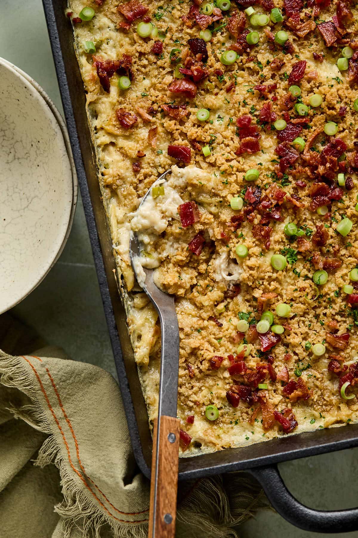 a spoon dipping into a million dollar chicken casserole topped with chopped bacon and green onions