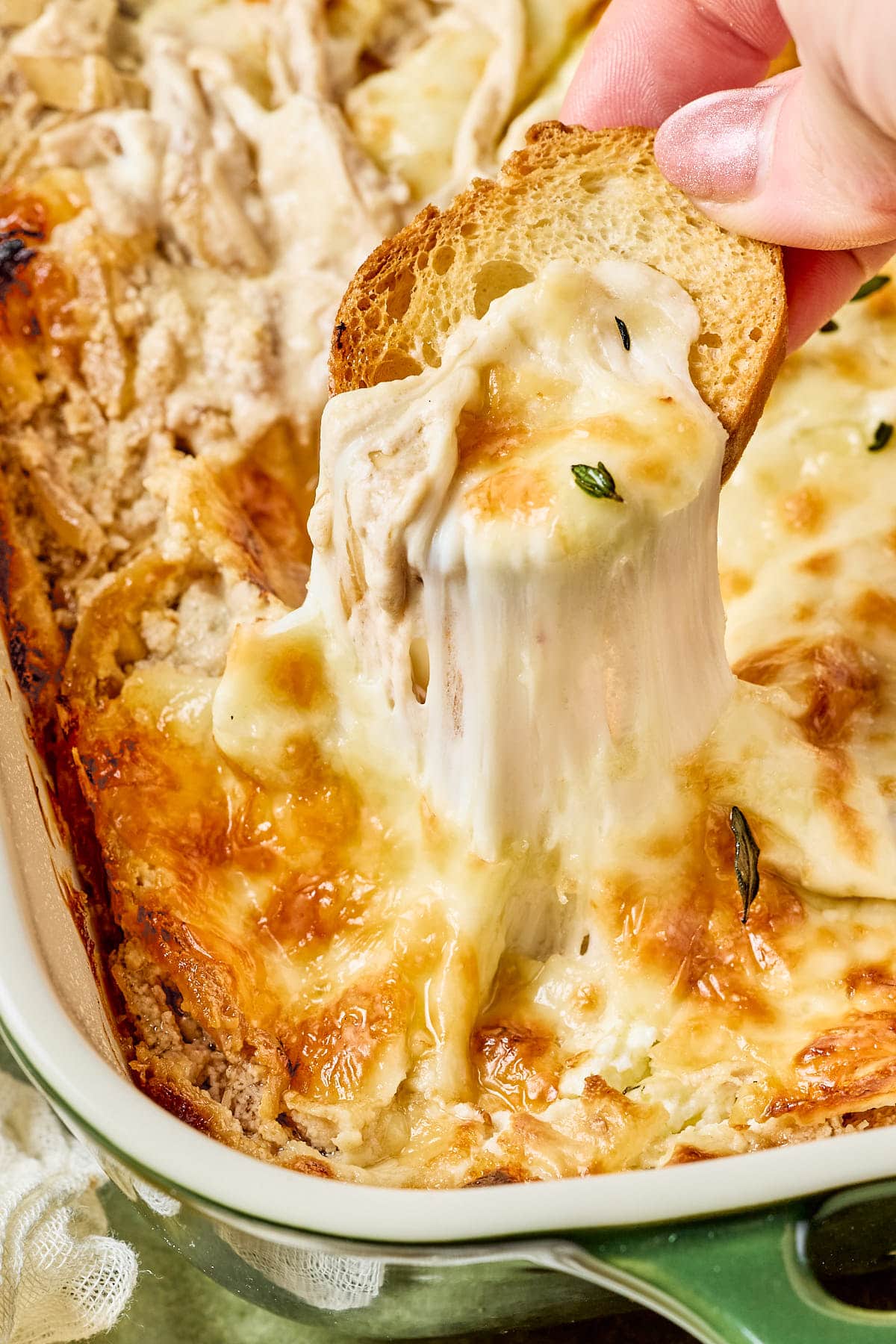 a hand dipping a crostini in greek yogurt french onion dip