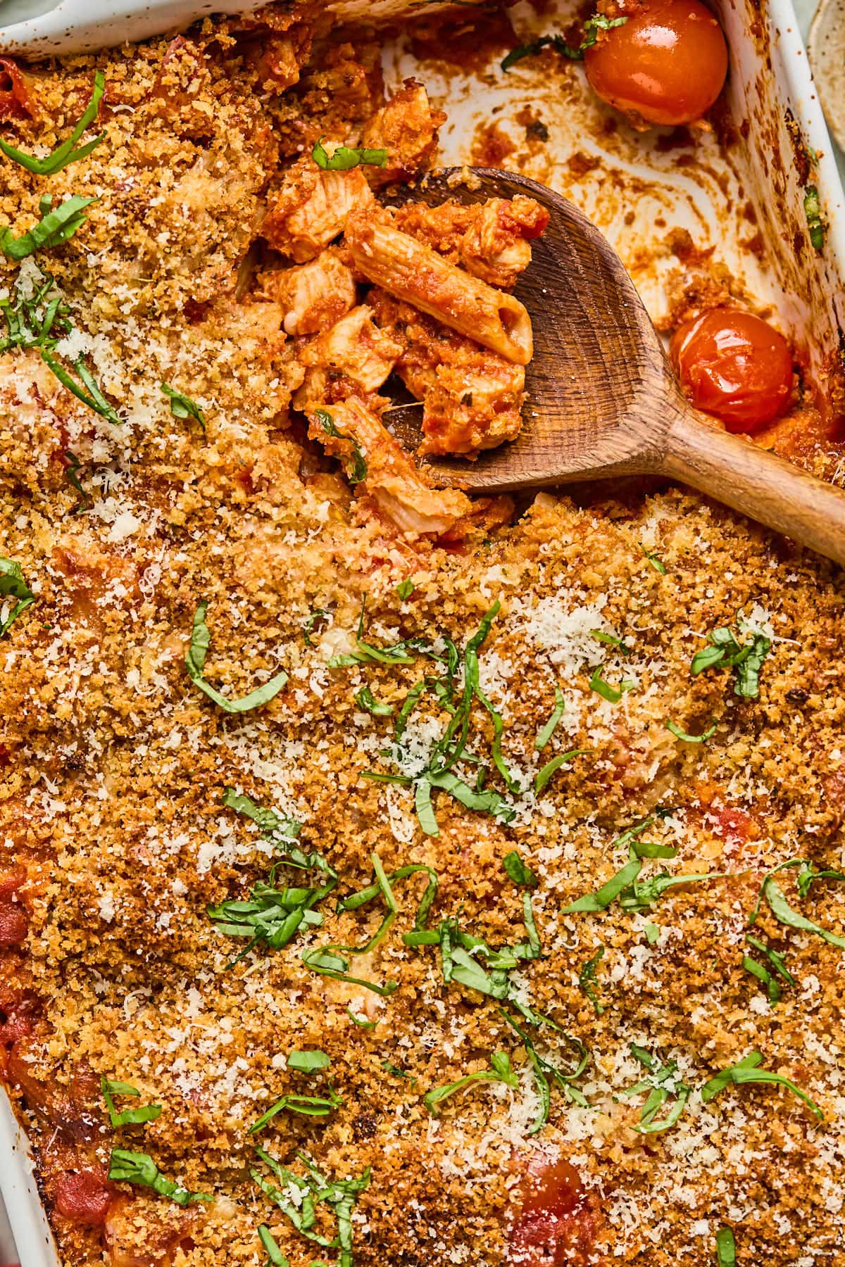 a wooden spoon scooping out chicken parmesan casserole from a baking dish 