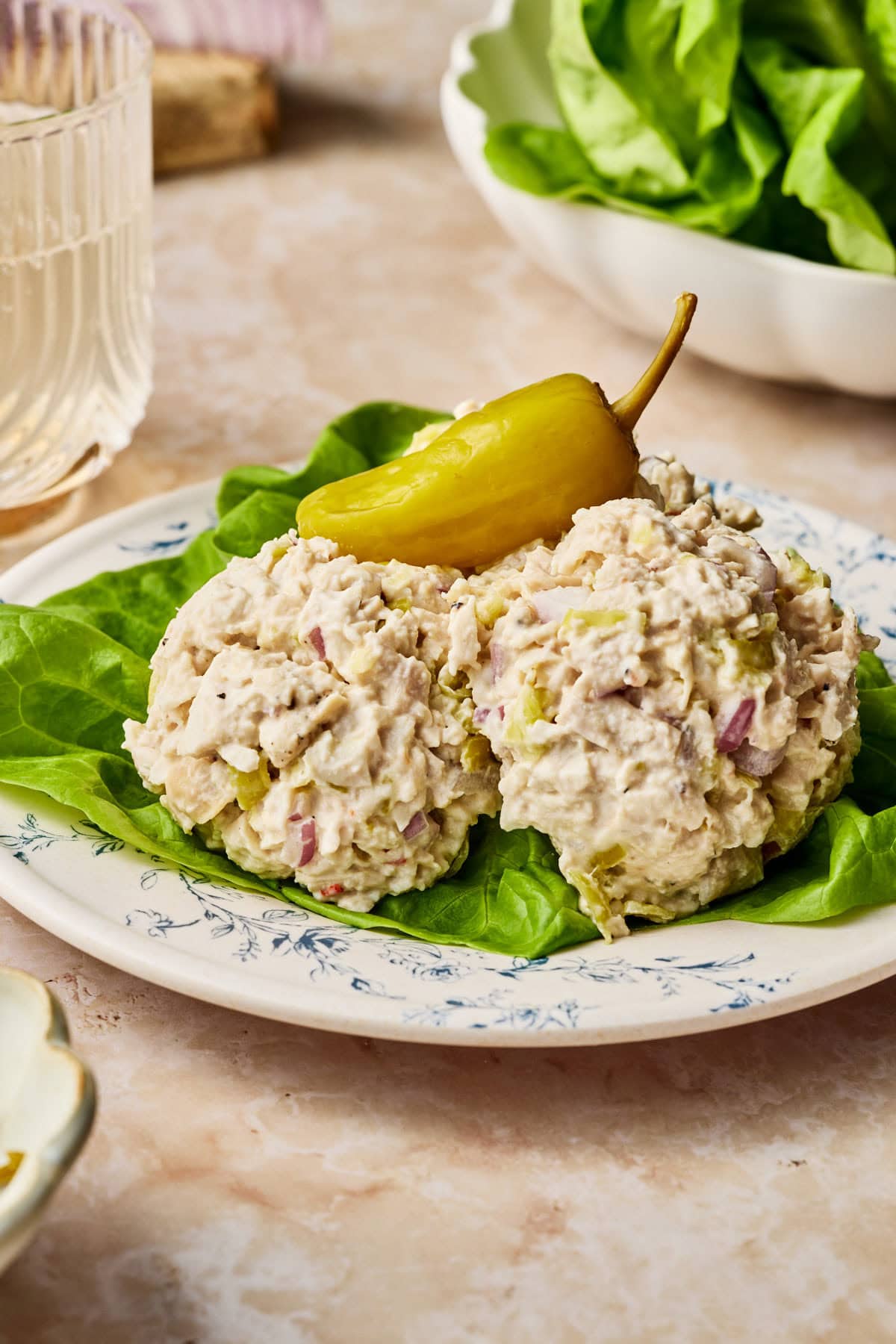 creamy pepperoncini chicken scooped on a bed of lettuce with a pepperoncni on top on a plate