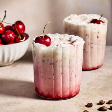 a cherry vanilla latte in a glass topped with frothy milk and a cherry