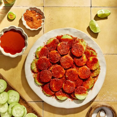 Mexican cucumbers on a white plate covered in hot sauce, lime juice, and tajin.