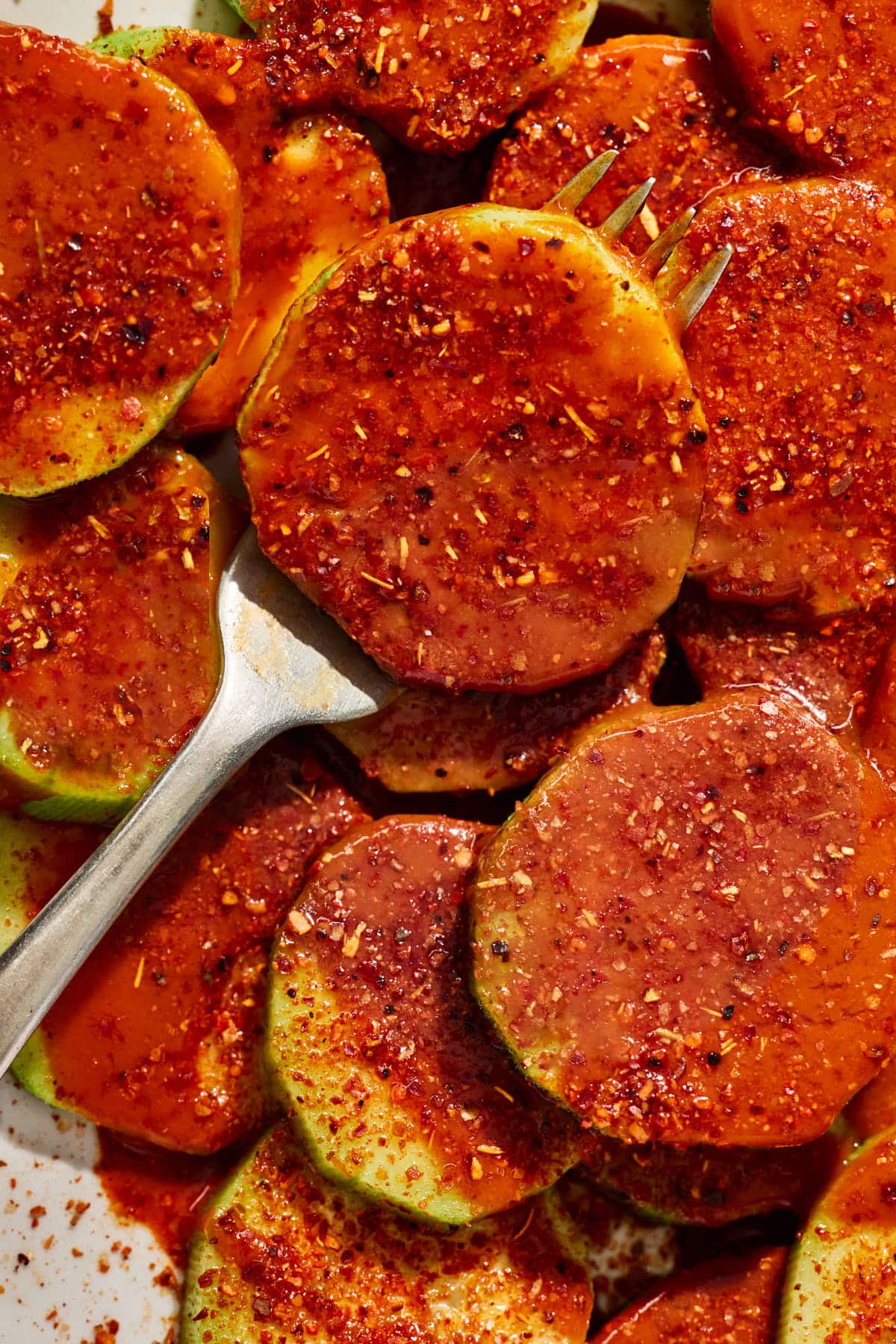 a fork lifting a cucumber covered in Mexican spices and hot sauce. 