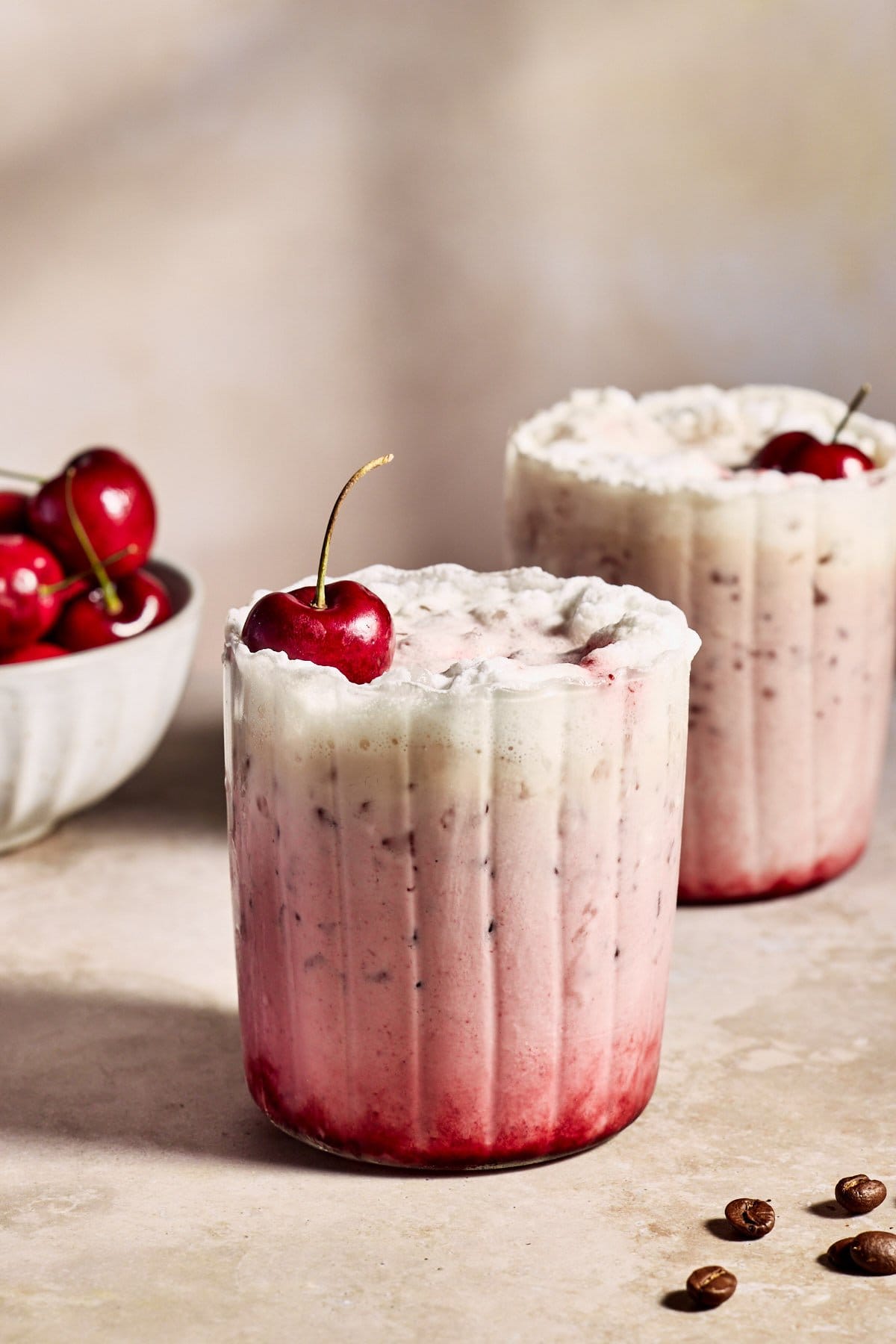 a close up of a cherry vanilla latte with cherry syrup, espresso, whipped cream, and a cherry