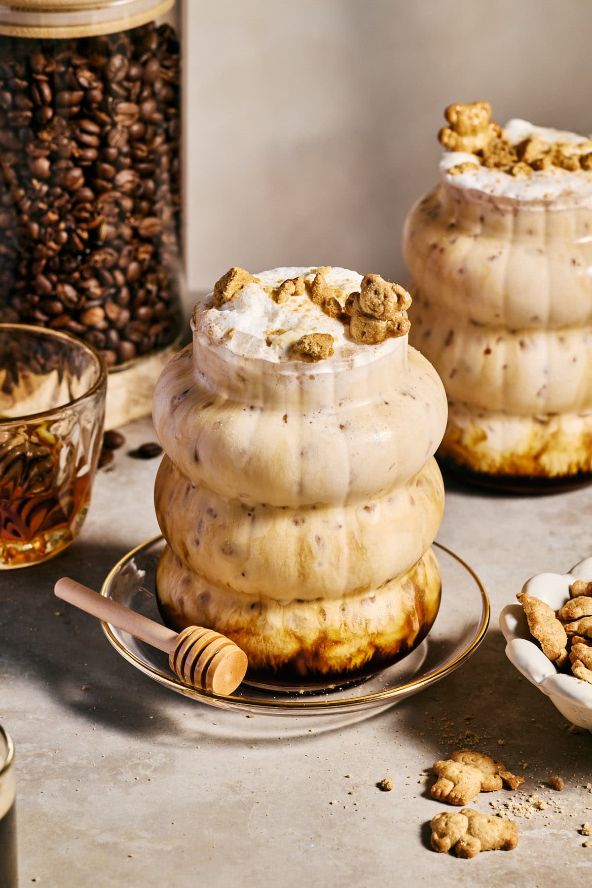 a teddy graham latte in a glass with ice topped with frothy milk