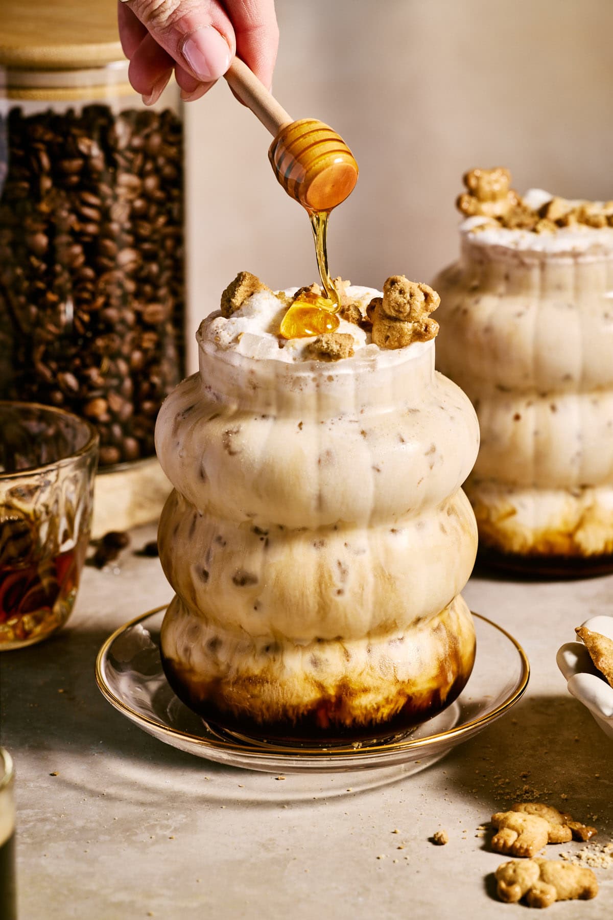a teddy graham latte in a glass with honey drizzling over the top