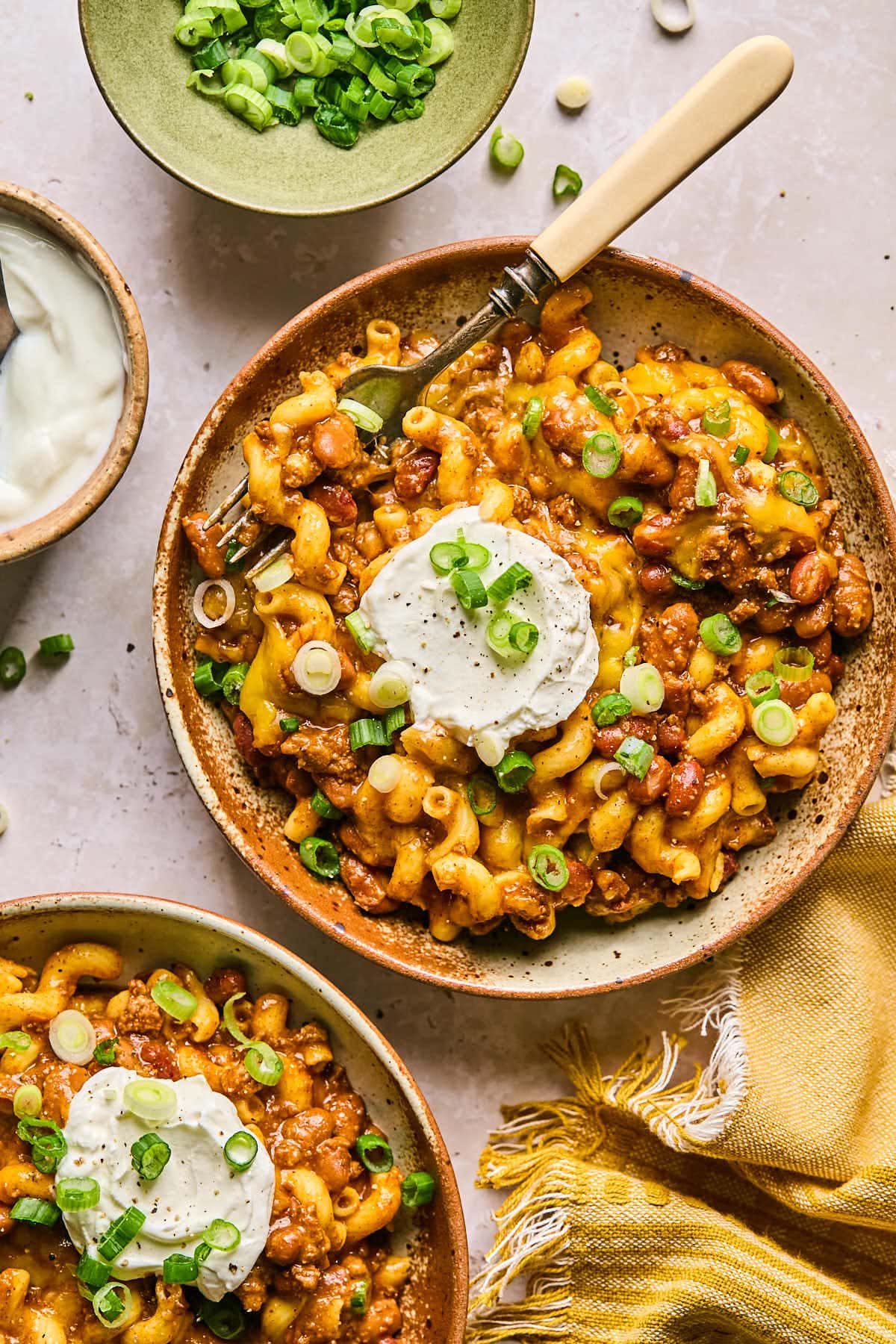 a bowl of chili mac topped with melted cheese and green onions and sour cream