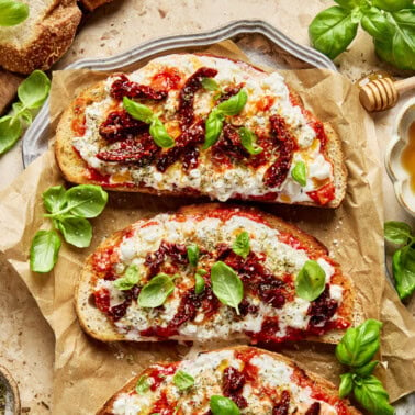 cottage cheese pizza toast on a a sheet of parchment topped with marinara, cottage cheese, sundried tomatoes and fresh basil and drizzled with hot honey