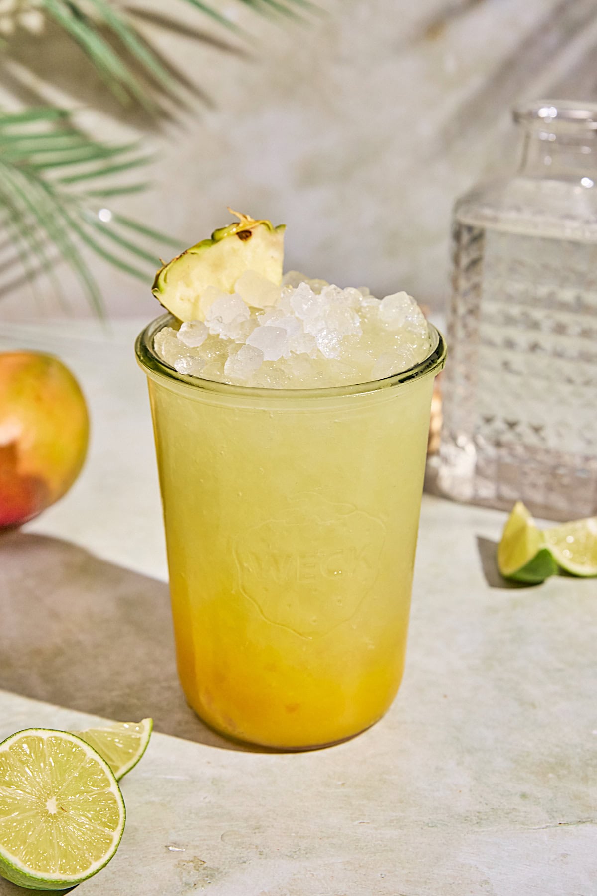 A golden yellow tropical mango pineapple Gatorade drink with layered mango and pineapple hues, served over ice in a clear glass and topped with a pineapple wedge. Fresh lime wedges are scattered around the glass. 