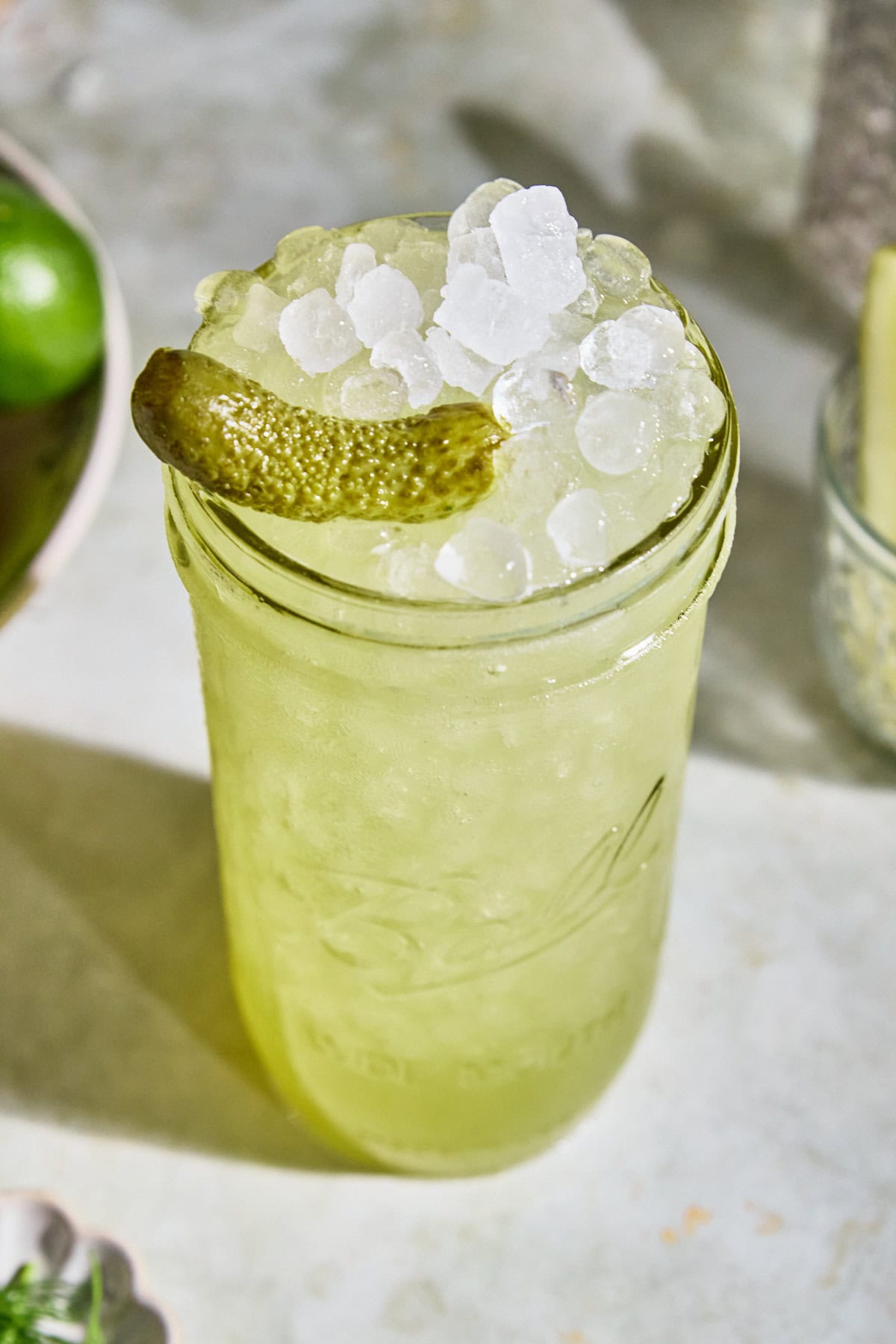 Close-up of a homemade dill pickle Gatorade served over ice with floating dill and a pickle spear garnish on a light surface.