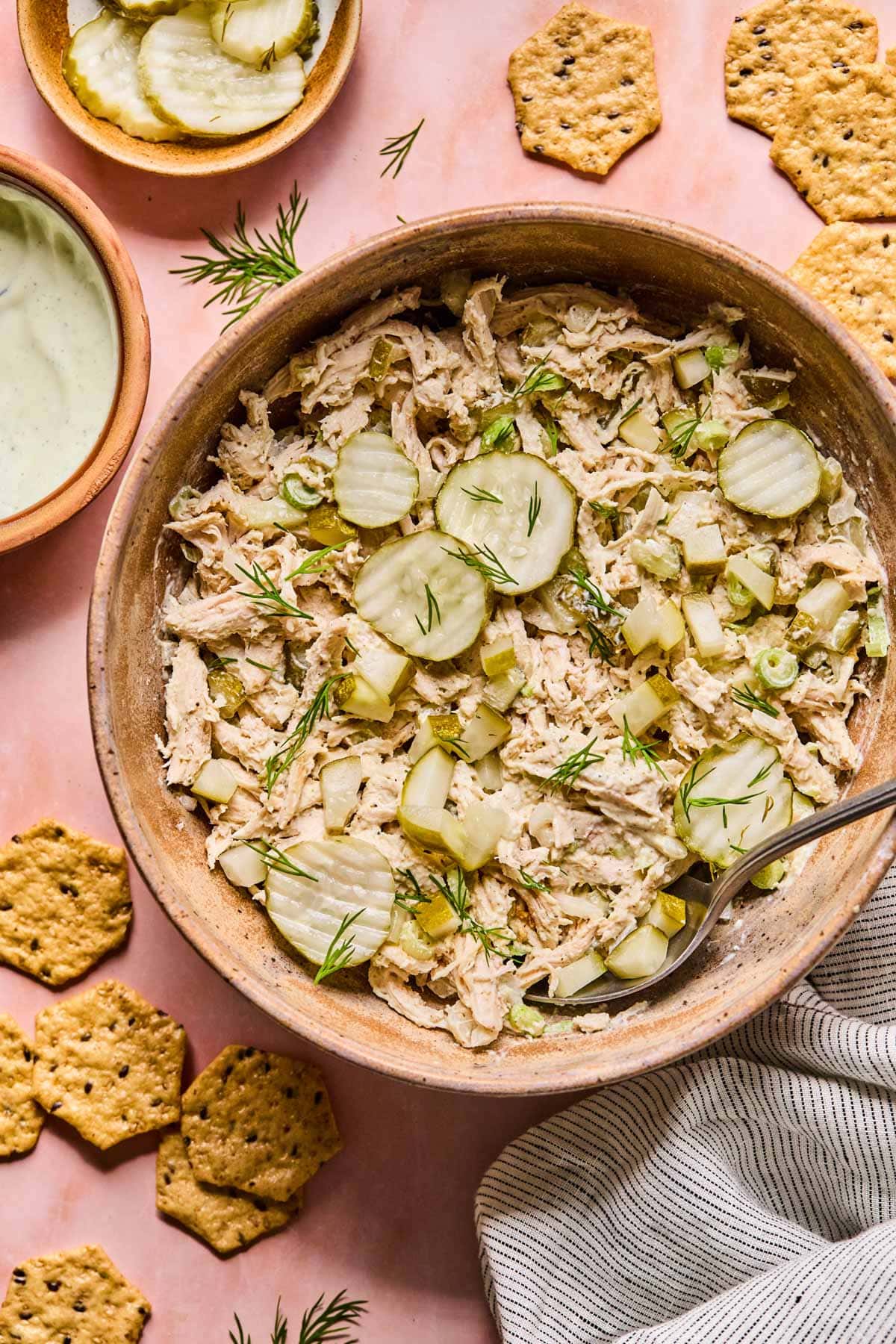 a wooden bowl filled with dill pickle chicken salad and topped with sliced pickled and fresh dill 