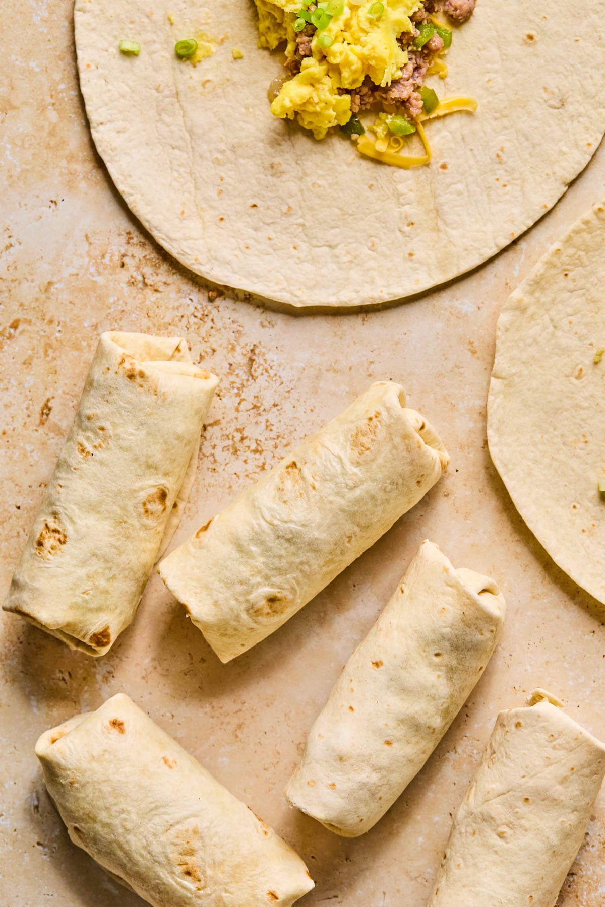 Tightly rolled breakfast burritos sitting on a light colored surface.