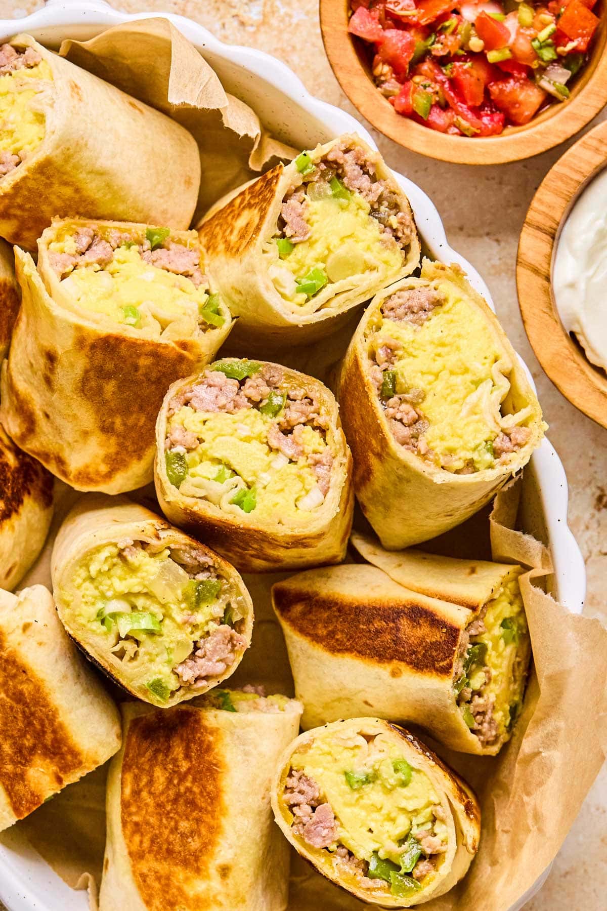 Close-up of halved breakfast burritos in a white ceramic dish, ready to freeze or eat.
