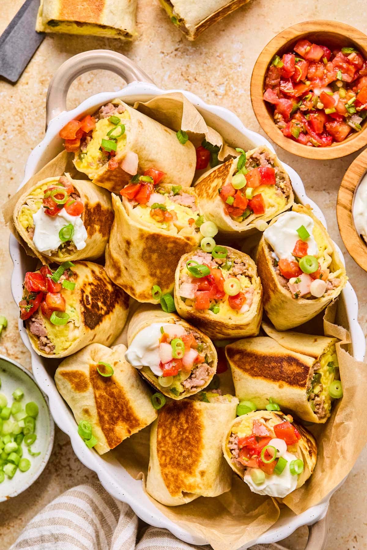 Freezer-friendly meal prep breakfast burritos cut in half showing eggs, sausage, and peppers in gluten-free tortillas in a ceramic white dish.