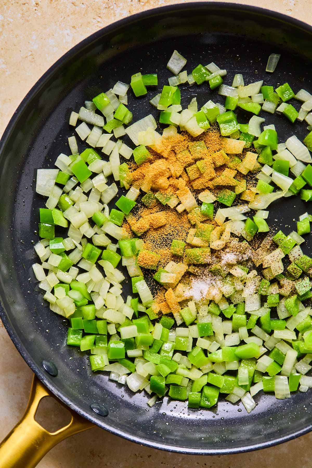 Bell pepper and onion sautéing in a skillet with oil and seasoning.