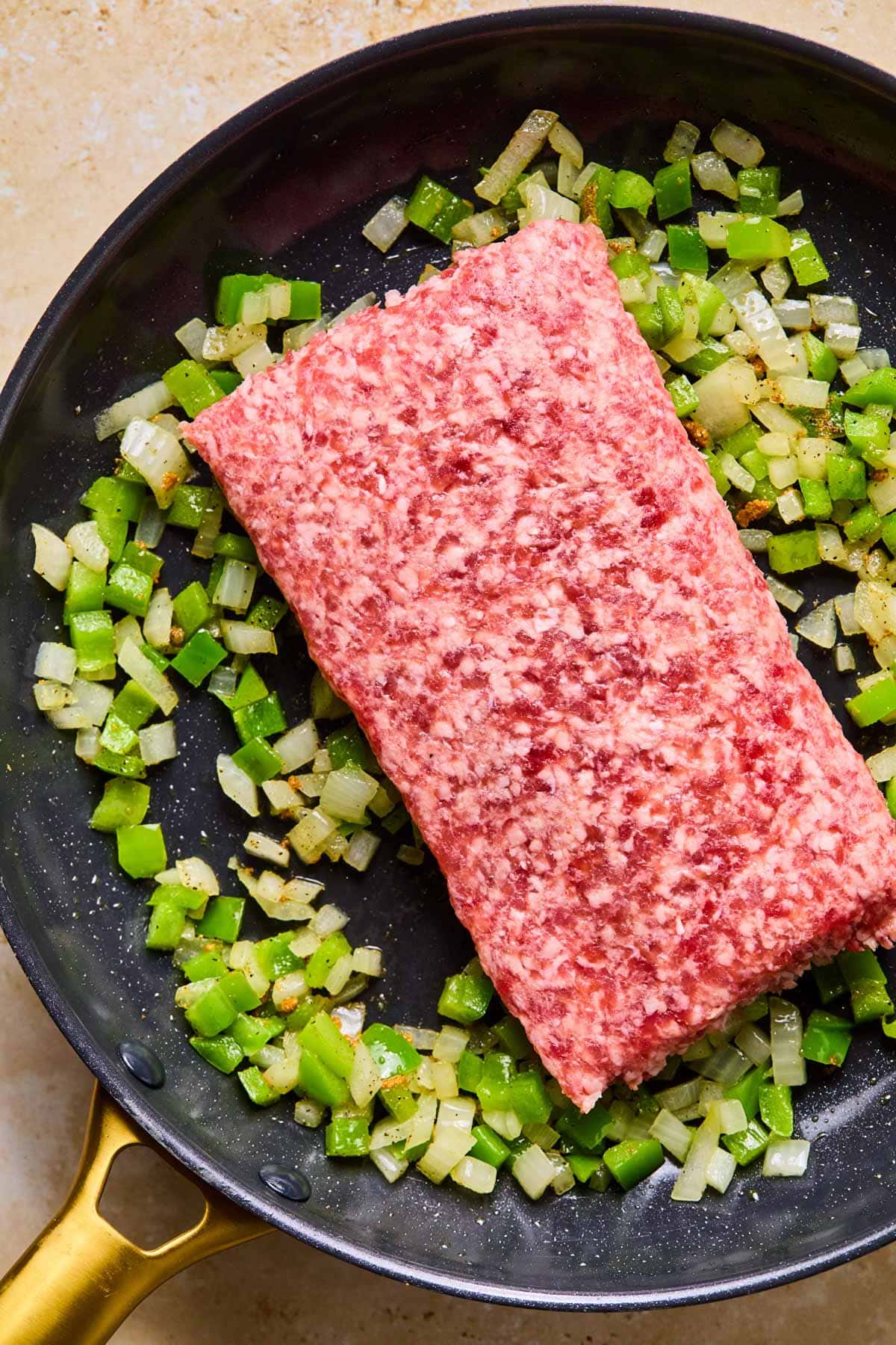 Raw breakfast sausage in a skillet with green pepper, onion, and seasoning, ready to brown.