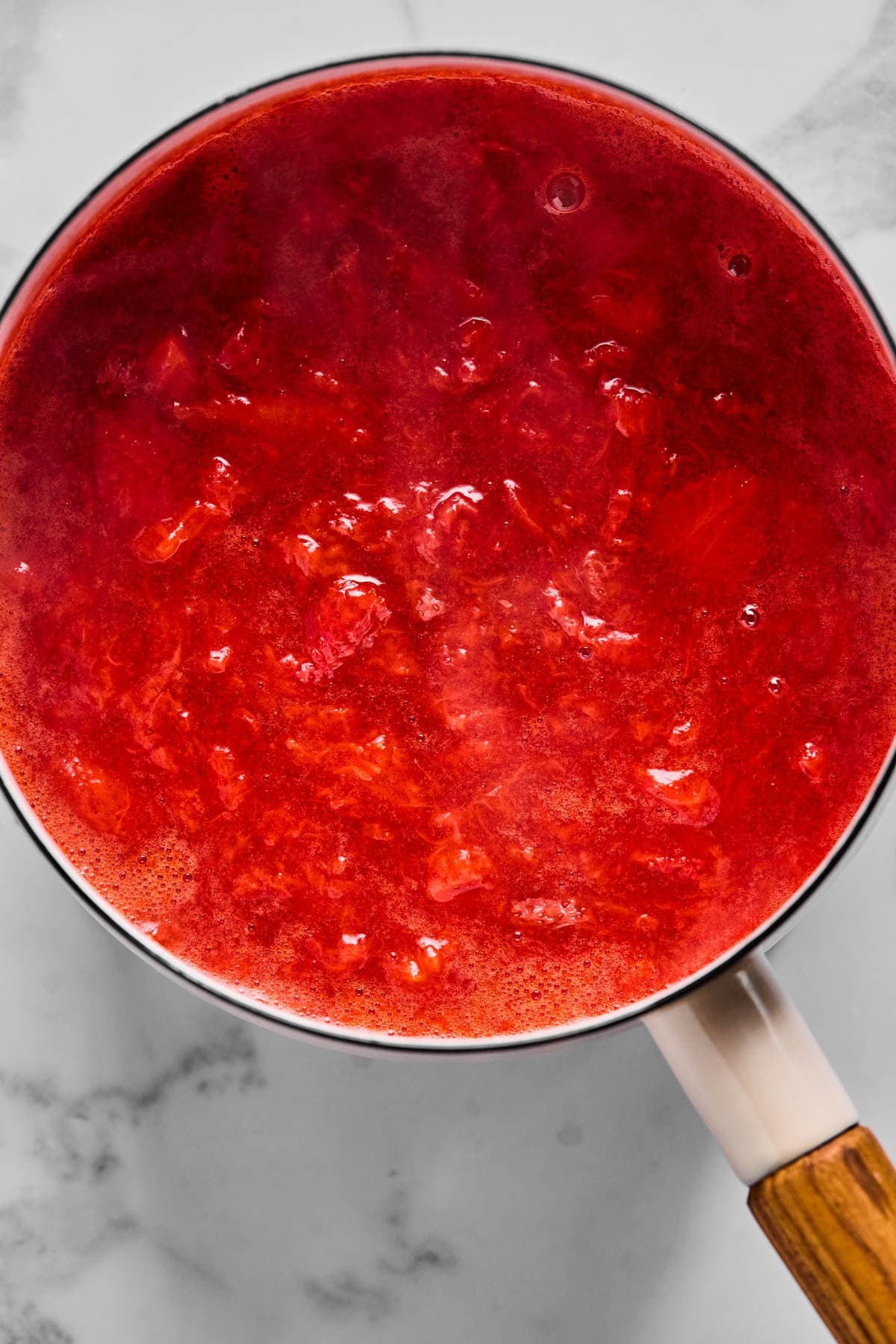 Fresh strawberries simmering in a pot, cooked down into homemade strawberry jam for layering in overnight oats.