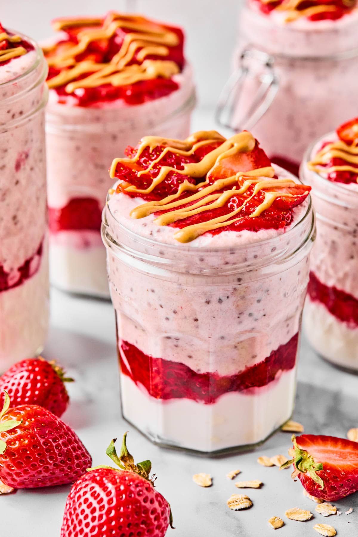 Close-up of a jar of chilled high protein overnight oats topped with fresh, sliced strawberries and drizzle of nut butter.